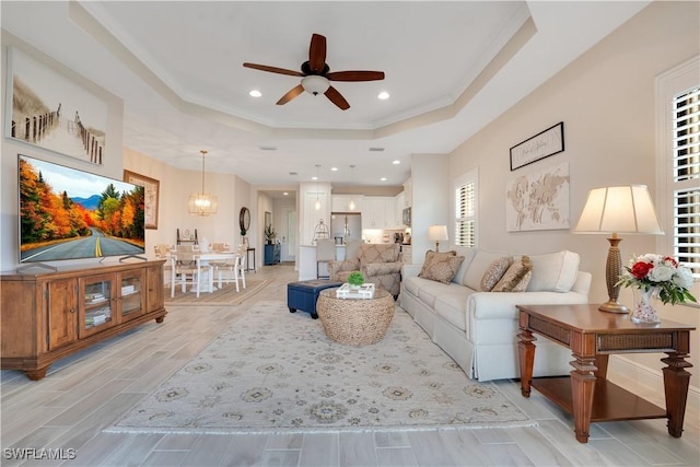 living area featuring ceiling fan with notable chandelier, a tray ceiling, wood finish floors, and recessed lighting