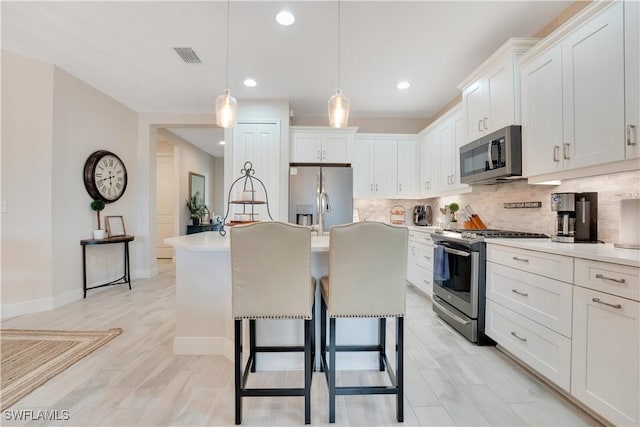 kitchen with white cabinets, a kitchen island with sink, stainless steel appliances, and light countertops