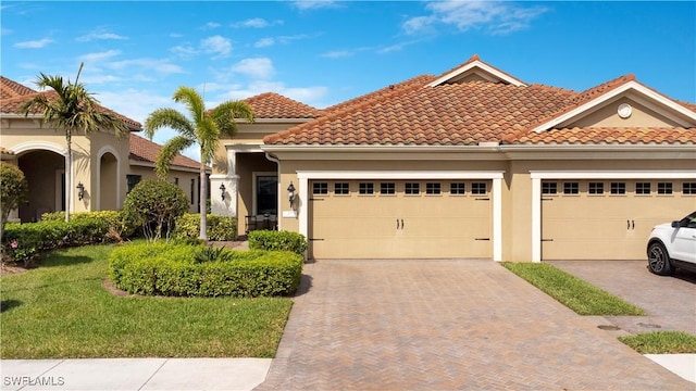 mediterranean / spanish home with decorative driveway, a tile roof, stucco siding, a front yard, and a garage