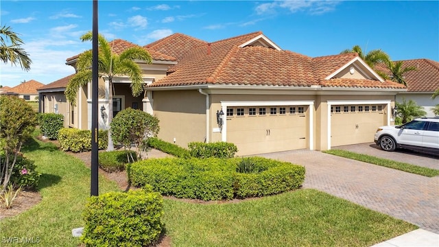 view of front of house featuring an attached garage, a tile roof, decorative driveway, stucco siding, and a front yard