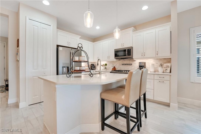 kitchen featuring tasteful backsplash, a center island with sink, white cabinets, stainless steel appliances, and light countertops