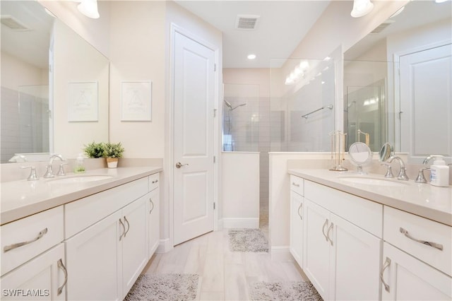 full bath featuring two vanities, visible vents, a walk in shower, and a sink