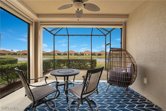 sunroom featuring a water view, a residential view, and a ceiling fan