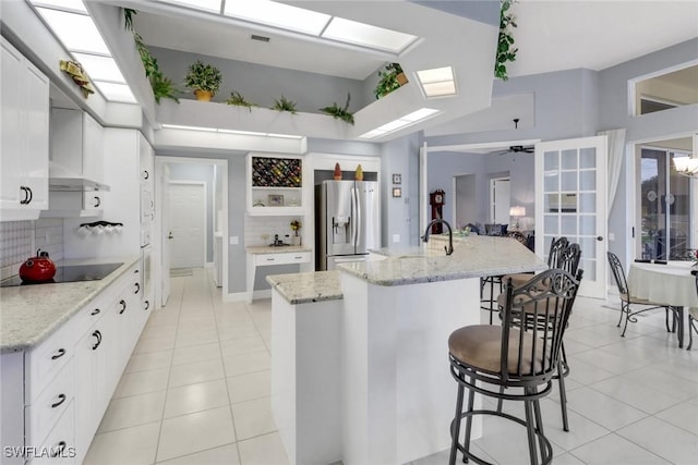 kitchen with a skylight, white cabinetry, an island with sink, stainless steel fridge, and black electric cooktop