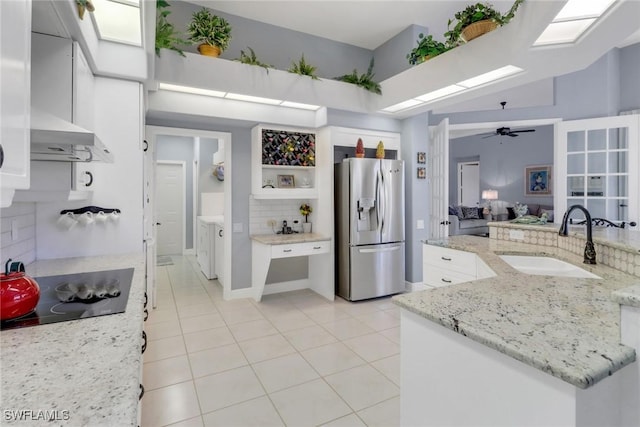 kitchen with light stone counters, black electric cooktop, a sink, white cabinetry, and stainless steel fridge