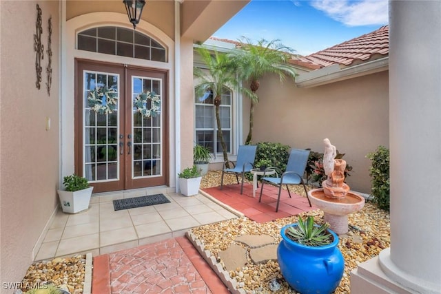 view of exterior entry with a patio area, french doors, a tile roof, and stucco siding