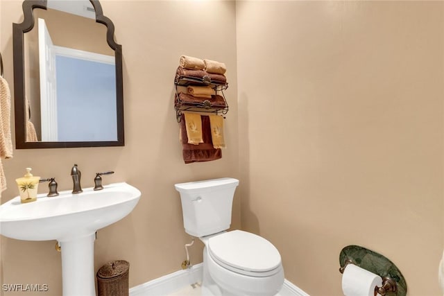 half bathroom featuring toilet, baseboards, and a sink