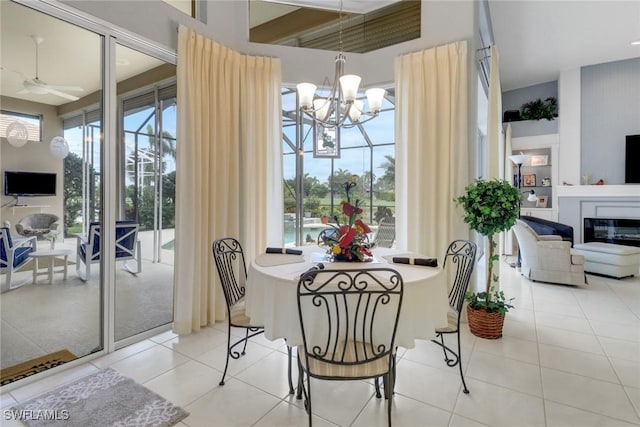 dining room with ceiling fan with notable chandelier, a glass covered fireplace, and light tile patterned floors