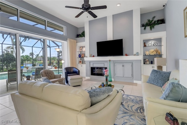 living room with light tile patterned floors, ceiling fan, built in shelves, a sunroom, and a glass covered fireplace