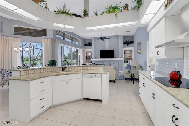 kitchen featuring a skylight, open floor plan, a sink, wall chimney range hood, and dishwasher