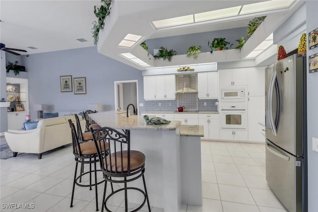 kitchen featuring white appliances, a skylight, white cabinetry, open floor plan, and wall chimney range hood