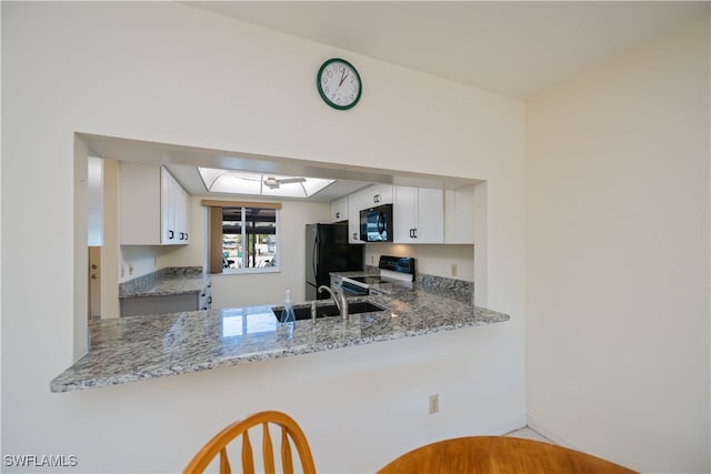 kitchen featuring a peninsula, range with electric cooktop, a sink, white cabinetry, and freestanding refrigerator