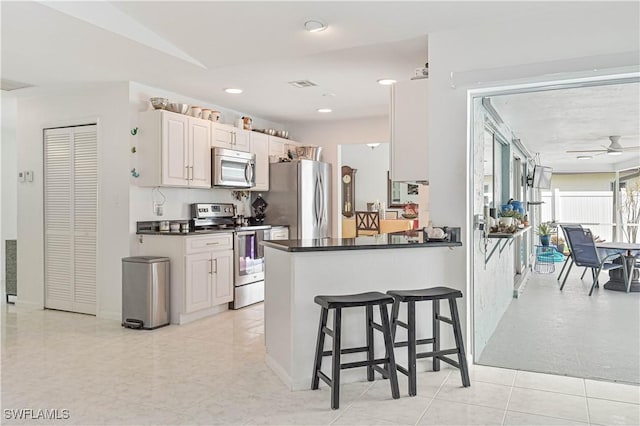 kitchen with white cabinets, dark countertops, appliances with stainless steel finishes, a breakfast bar, and a peninsula