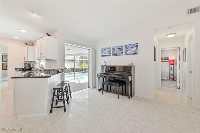 kitchen featuring visible vents, white cabinets, dark countertops, a kitchen breakfast bar, and a peninsula