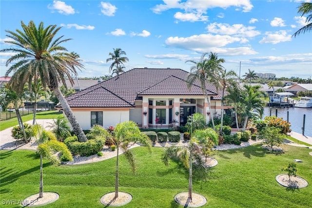 mediterranean / spanish-style house featuring a water view, a tiled roof, a front lawn, and stucco siding