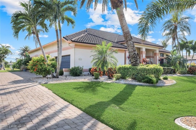 view of front of house with a front yard, an attached garage, a tile roof, and stucco siding