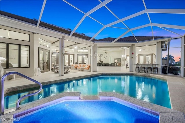 pool at dusk featuring a lanai, a patio area, french doors, and an outdoor hangout area