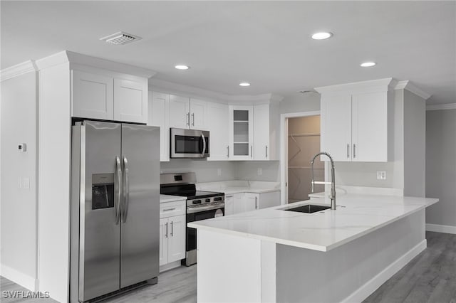 kitchen with appliances with stainless steel finishes, glass insert cabinets, white cabinets, a sink, and a peninsula