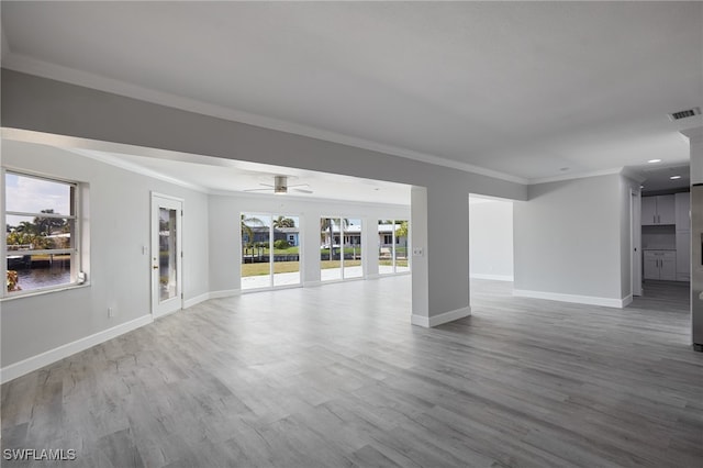 unfurnished living room featuring baseboards, wood finished floors, visible vents, and crown molding