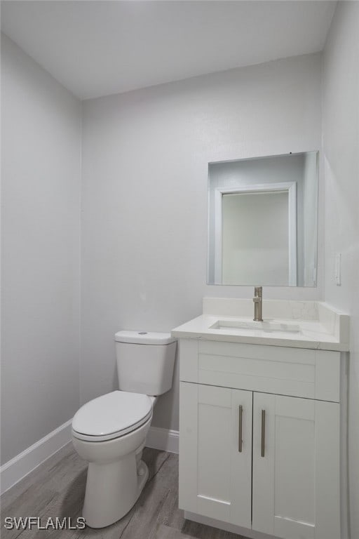 half bath with baseboards, vanity, toilet, and wood finished floors