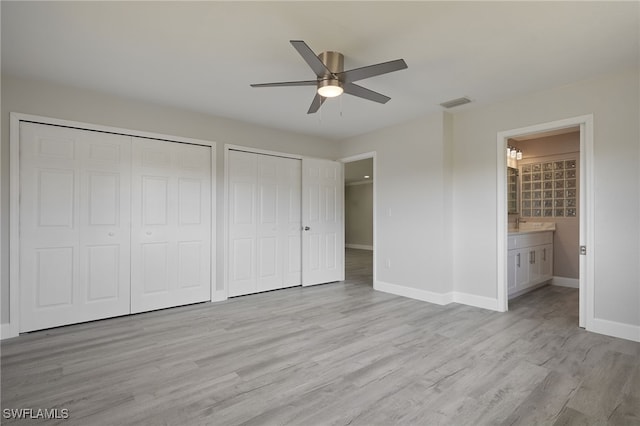 unfurnished bedroom featuring multiple closets, ensuite bath, light wood-style flooring, and baseboards