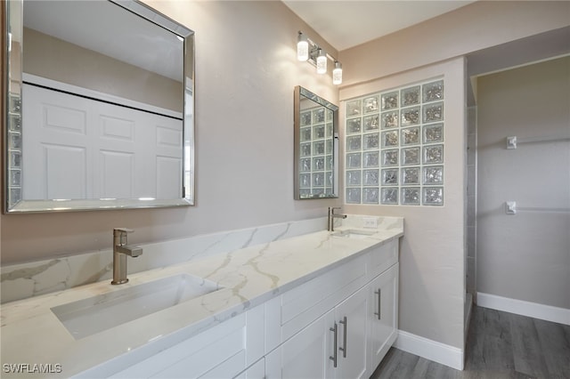 full bath featuring double vanity, wood finished floors, a sink, and baseboards