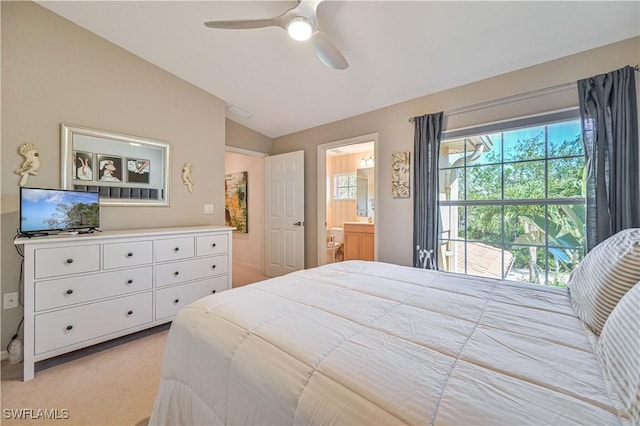 bedroom featuring a ceiling fan, light colored carpet, vaulted ceiling, and ensuite bath