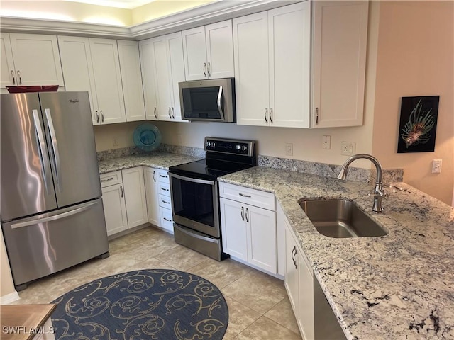 kitchen featuring appliances with stainless steel finishes, a peninsula, light stone countertops, white cabinetry, and a sink