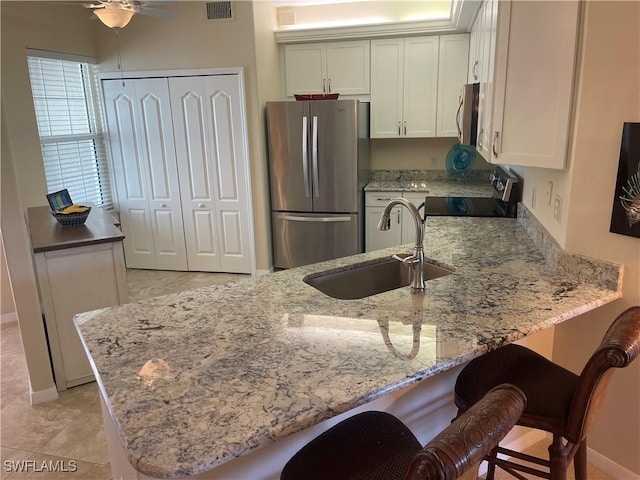 kitchen with light stone counters, stainless steel appliances, white cabinets, a sink, and a peninsula