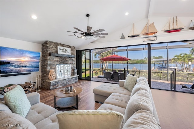 living area with lofted ceiling, a fireplace, wood finished floors, a ceiling fan, and a water view