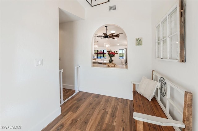 corridor with arched walkways, wood finished floors, visible vents, and baseboards