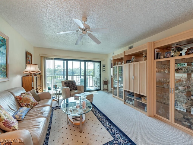 living area with ceiling fan, visible vents, a textured ceiling, and light colored carpet