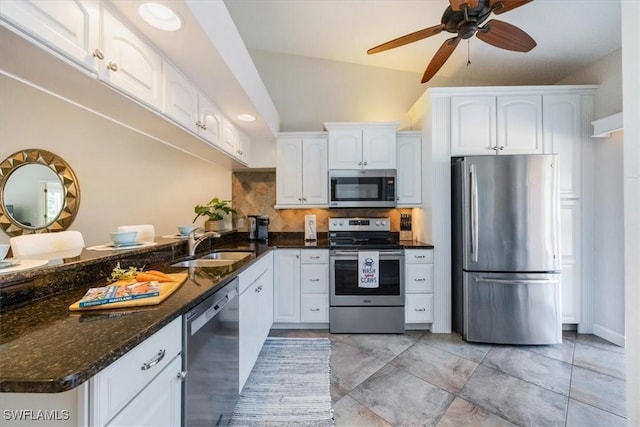 kitchen featuring a peninsula, a sink, white cabinets, appliances with stainless steel finishes, and dark stone counters