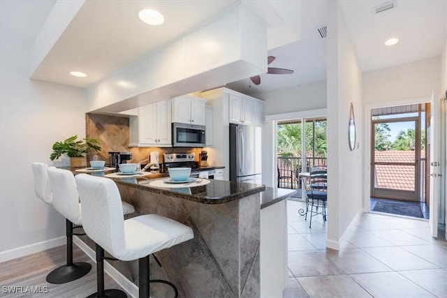 kitchen with a breakfast bar area, stainless steel appliances, baseboards, white cabinets, and tasteful backsplash