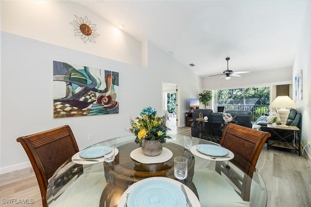 dining space featuring high vaulted ceiling, ceiling fan, light wood-style flooring, and baseboards