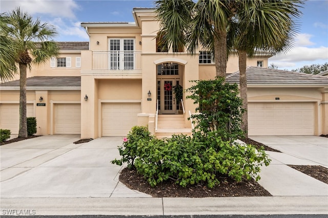 view of front facade featuring stucco siding, driveway, a tile roof, french doors, and a balcony