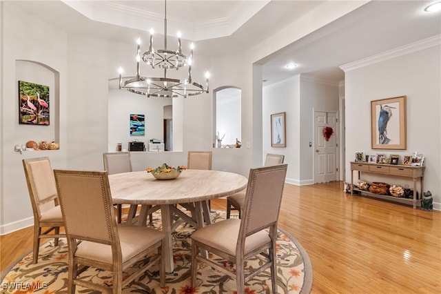 dining area featuring light wood-style flooring, ornamental molding, a tray ceiling, arched walkways, and baseboards