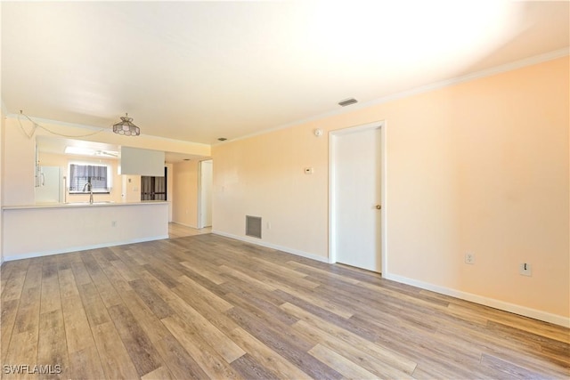 unfurnished living room featuring baseboards, visible vents, crown molding, and light wood finished floors