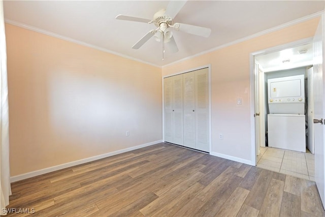 unfurnished bedroom with light wood-style flooring, a closet, crown molding, and stacked washer and clothes dryer