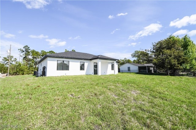 rear view of property with a yard, fence, and stucco siding