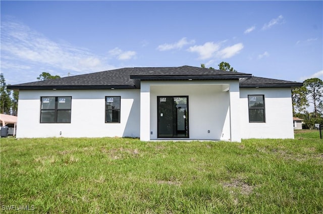 back of property with a shingled roof, a lawn, and stucco siding