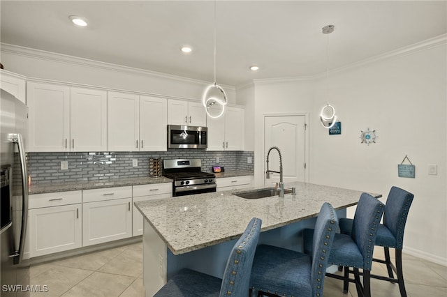 kitchen featuring a kitchen island with sink, a sink, white cabinets, appliances with stainless steel finishes, and pendant lighting