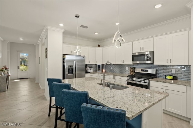 kitchen with appliances with stainless steel finishes, a kitchen island with sink, white cabinetry, pendant lighting, and a sink