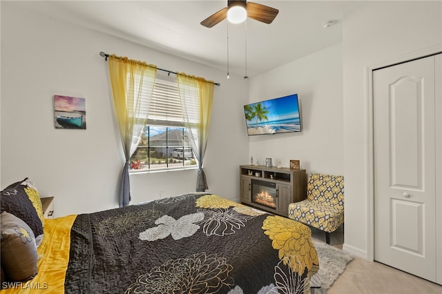 bedroom featuring a ceiling fan, a glass covered fireplace, and light tile patterned floors