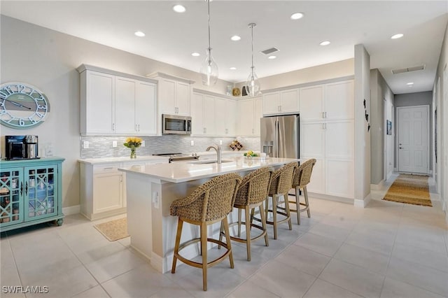 kitchen with tasteful backsplash, a center island with sink, visible vents, appliances with stainless steel finishes, and a kitchen bar