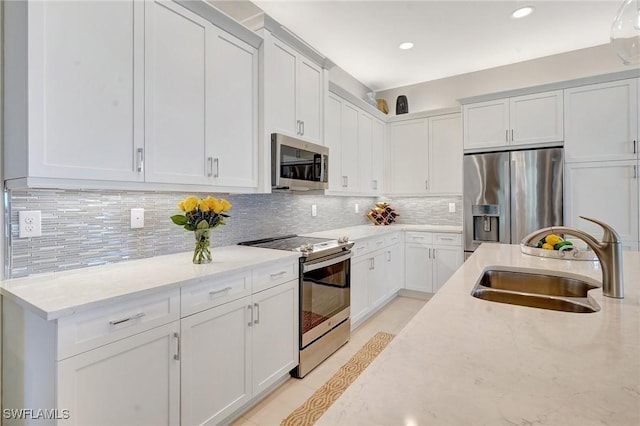 kitchen with a sink, light stone countertops, stainless steel appliances, white cabinetry, and backsplash