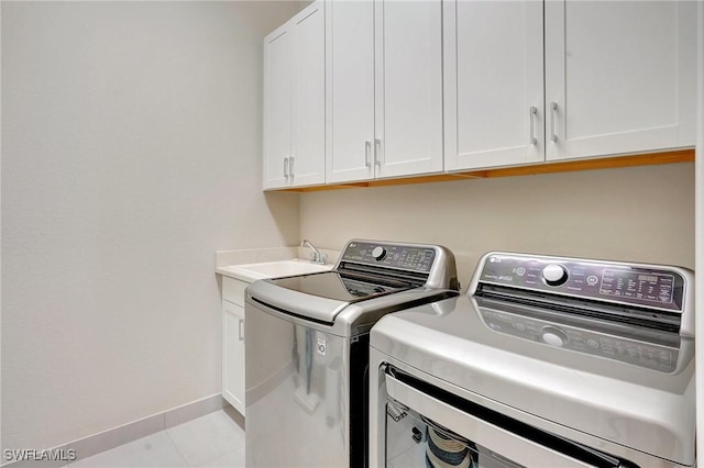 washroom featuring light tile patterned floors, cabinet space, baseboards, washing machine and clothes dryer, and a sink