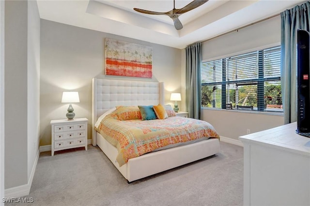 bedroom with light carpet, baseboards, and a tray ceiling