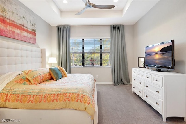 carpeted bedroom featuring a tray ceiling, ceiling fan, and baseboards