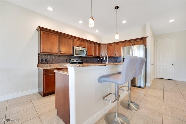 kitchen with brown cabinets, light tile patterned floors, stainless steel appliances, hanging light fixtures, and a kitchen island with sink